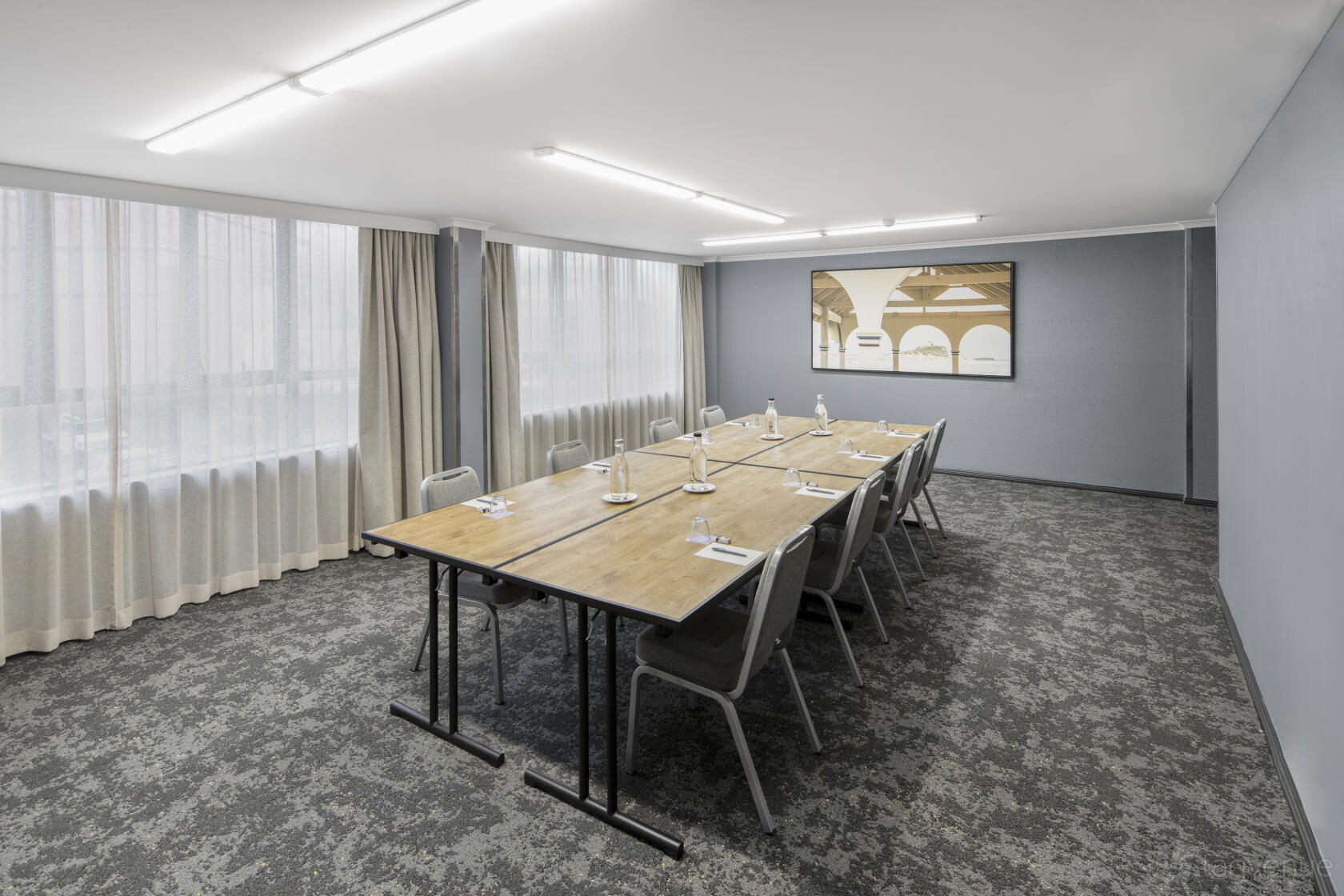 A boardroom with a long wooden meeting table, grey chairs, and large windows with sheer curtains at Mercure Newcastle.