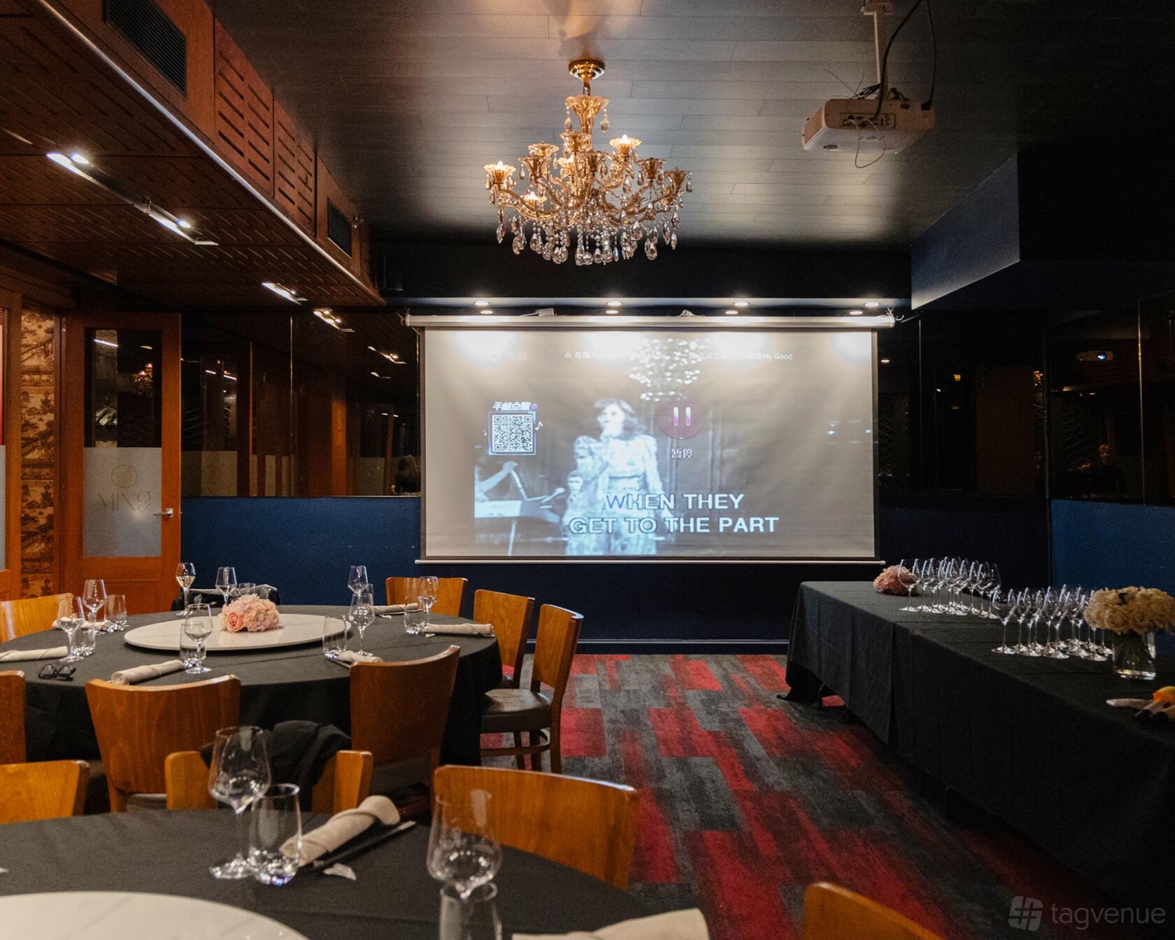 An event space with a crystal chandelier, projection screen, and set dining tables at Ming Dining Restaurant & Bar.