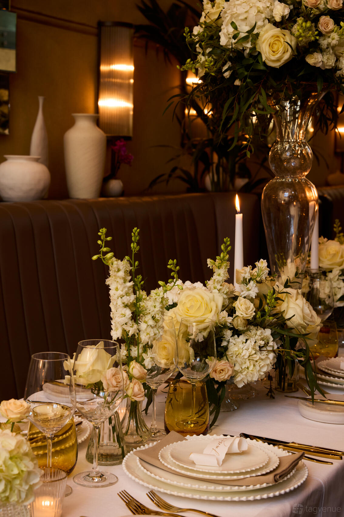 A restaurant with floral centerpieces, a lit taper candle, and upholstered banquette seating at Galvin La Chapelle.