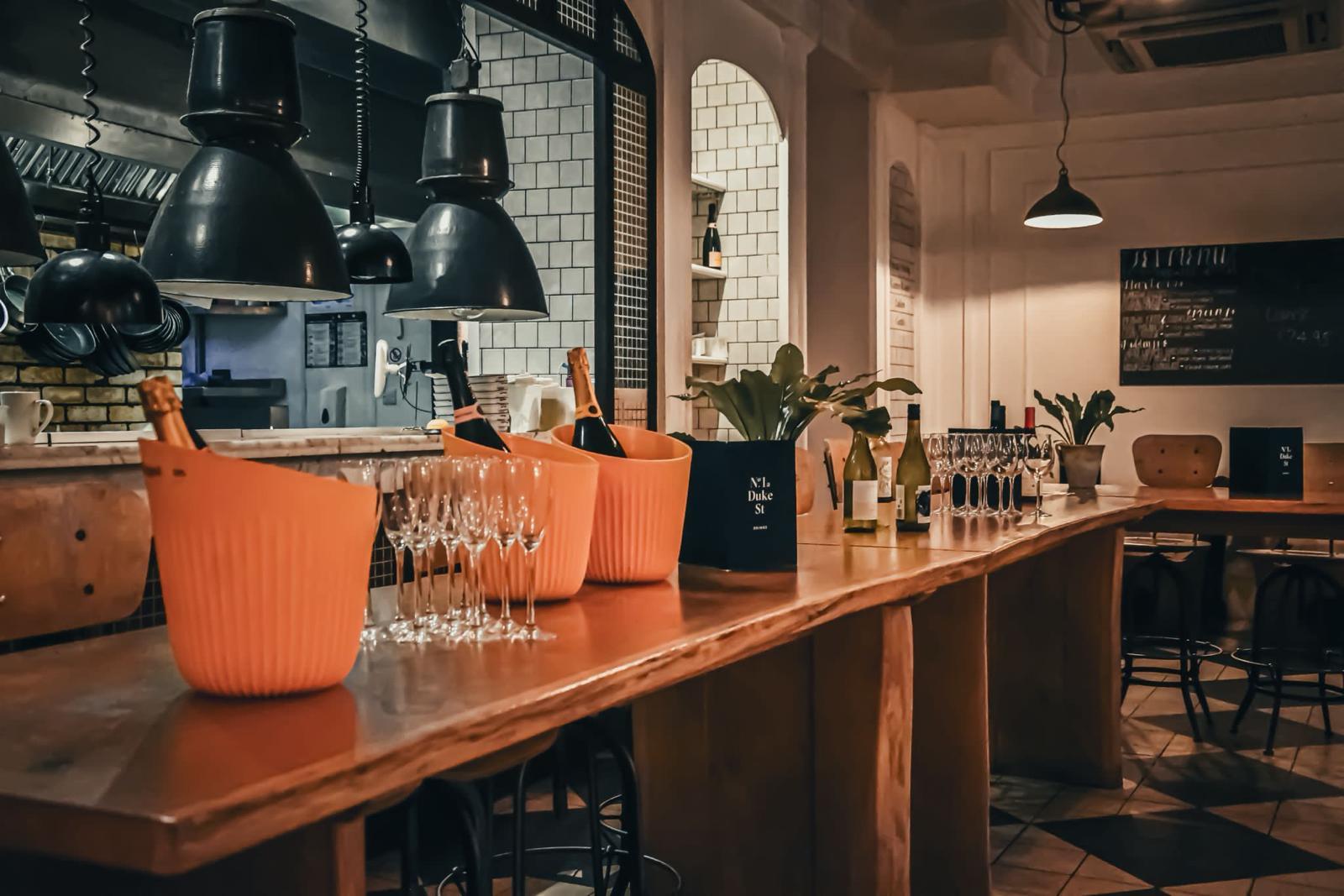 An event space with pendant lighting, high wooden counter, wine buckets, glassware, and potted plants at No.1 Duke Street.