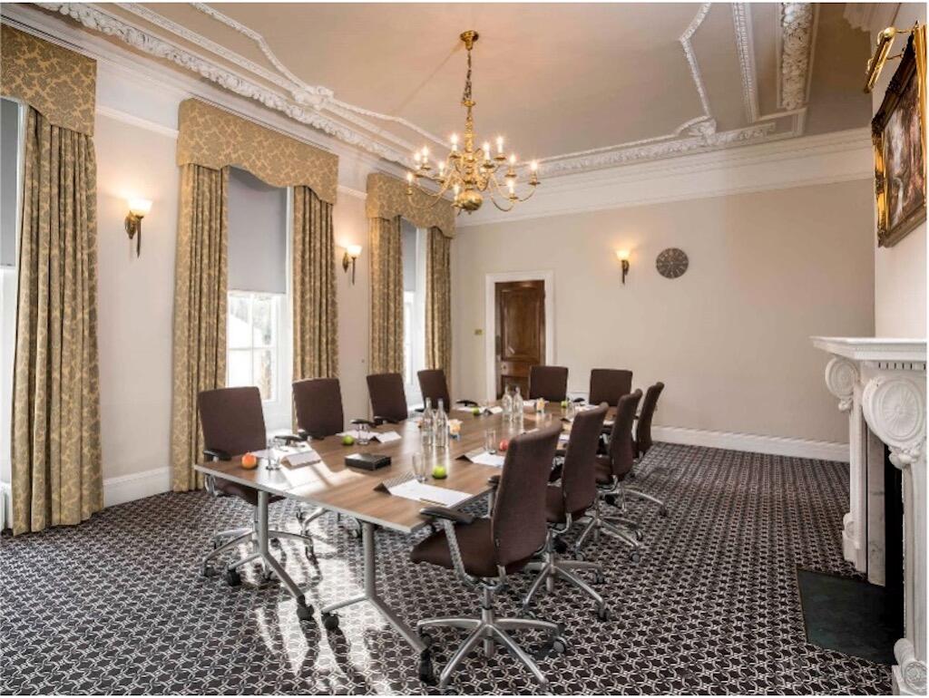 A meeting room with a long table, brown chairs, chandelier lighting, and ornate curtains at Hunton Park Hotel.