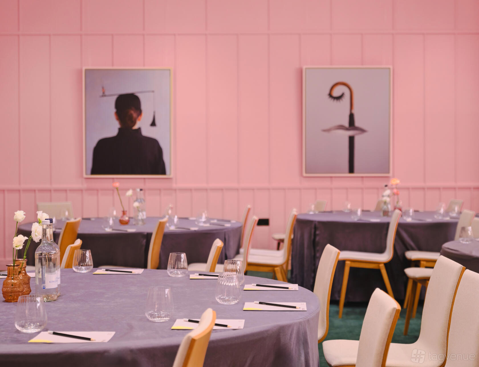 An event space with round tables, grey tablecloths, modern chairs, and pink-paneled walls with framed art at art'otel London Battersea Power Station.