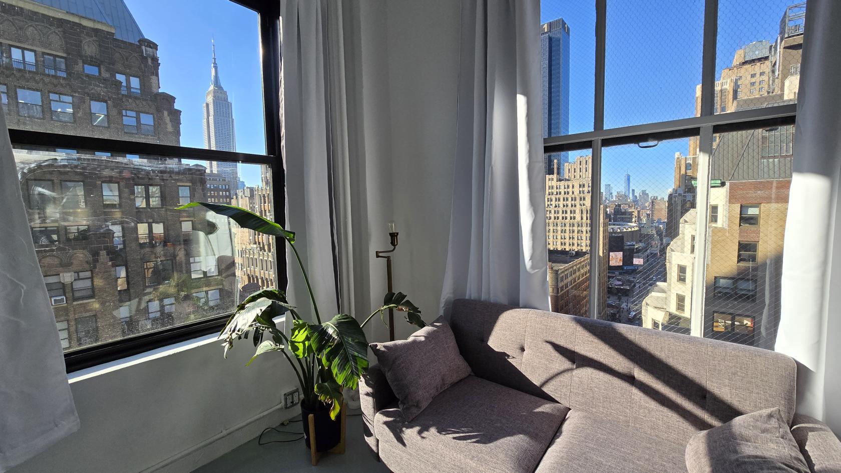 A photo studio in a loft with large corner windows, white curtains, and a view of the Empire State Building at Production Loft.
