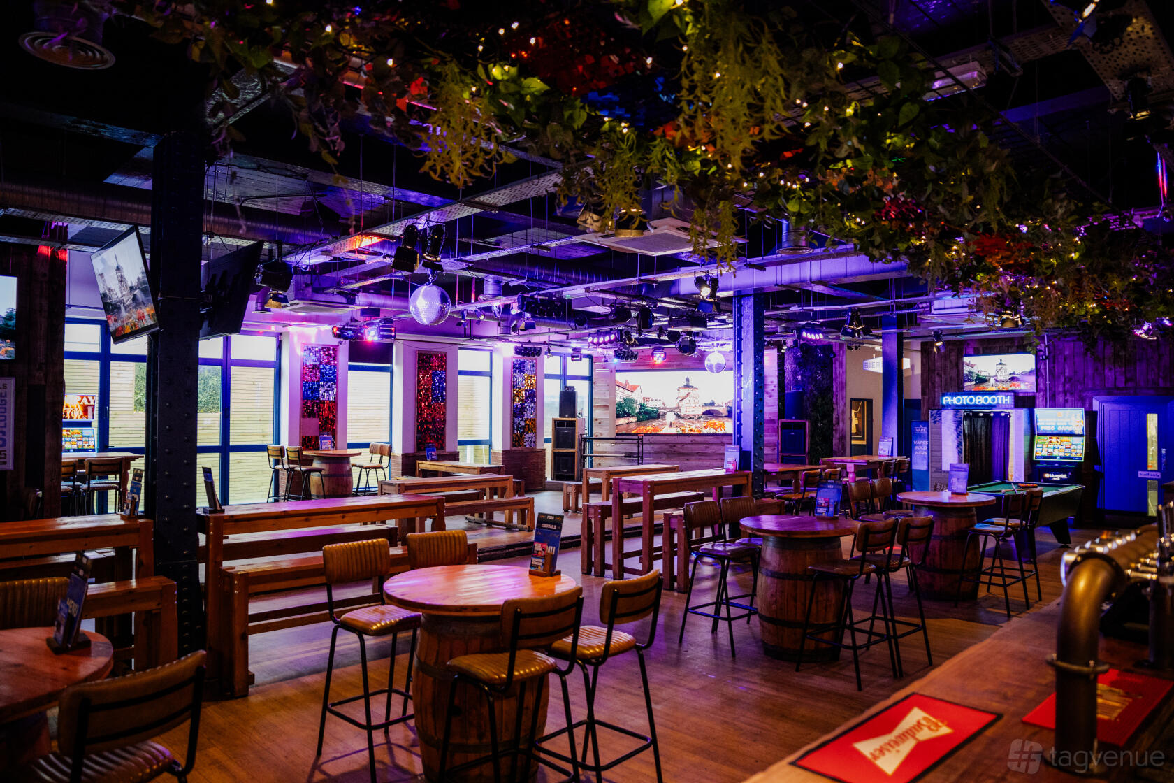 An event space in a bar with wooden tables, barrel seating, hanging greenery, and neon lighting at The Bierkeller Nottingham.