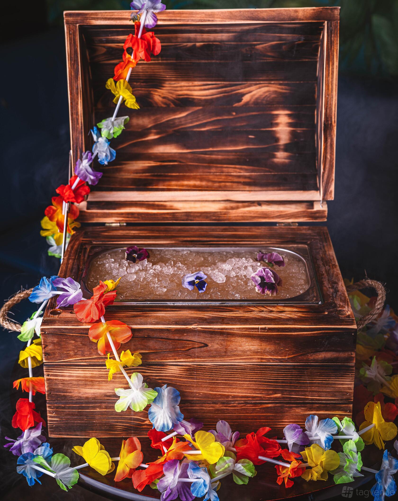 A tiki event space with a wooden ice chest, tropical flowers, and decorative leis at Tiki Hideaway Liverpool.