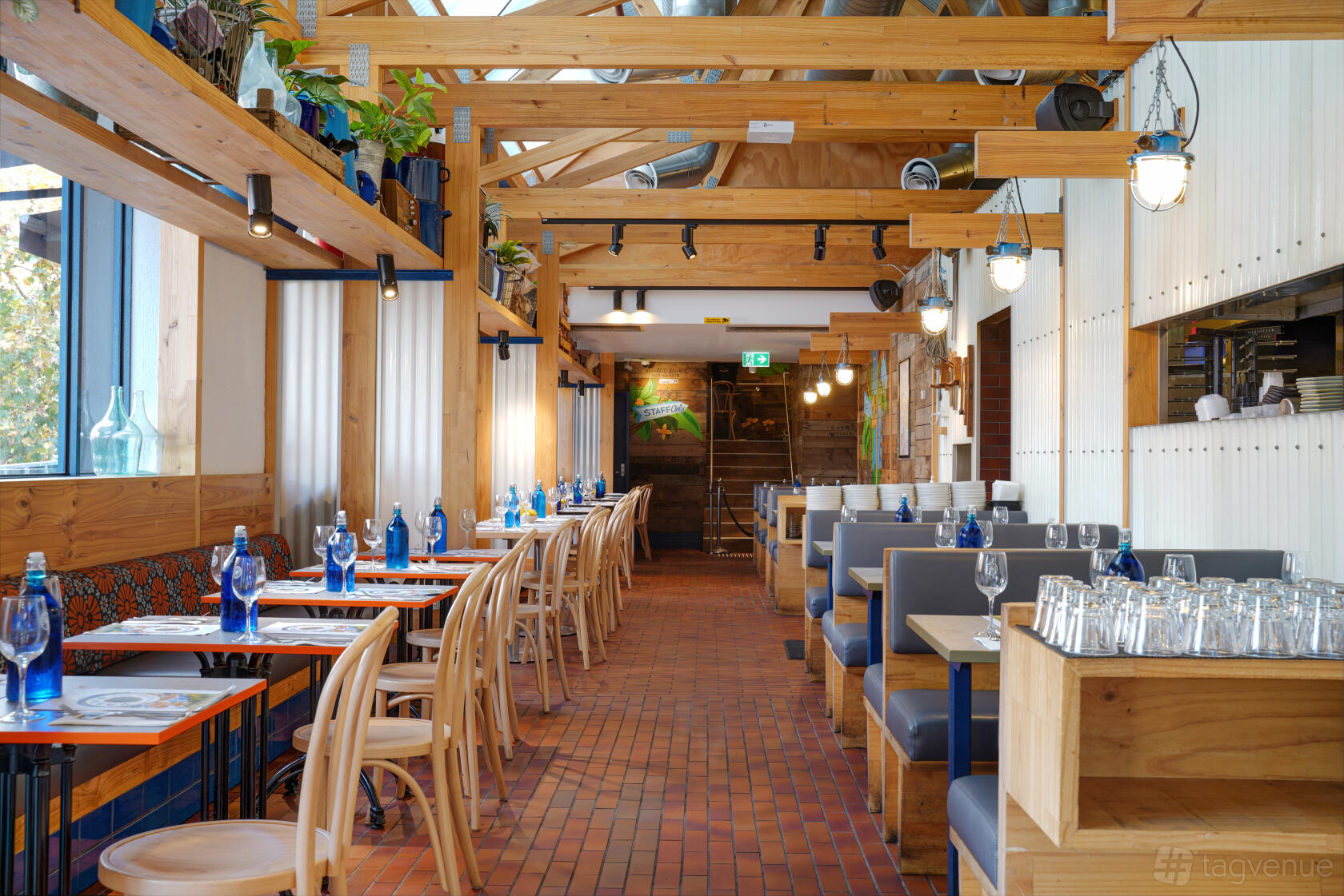 A restaurant with wooden beams, blue glass bottles on tables, and booth seating at YASSAS - The Greek Way - Eastland.