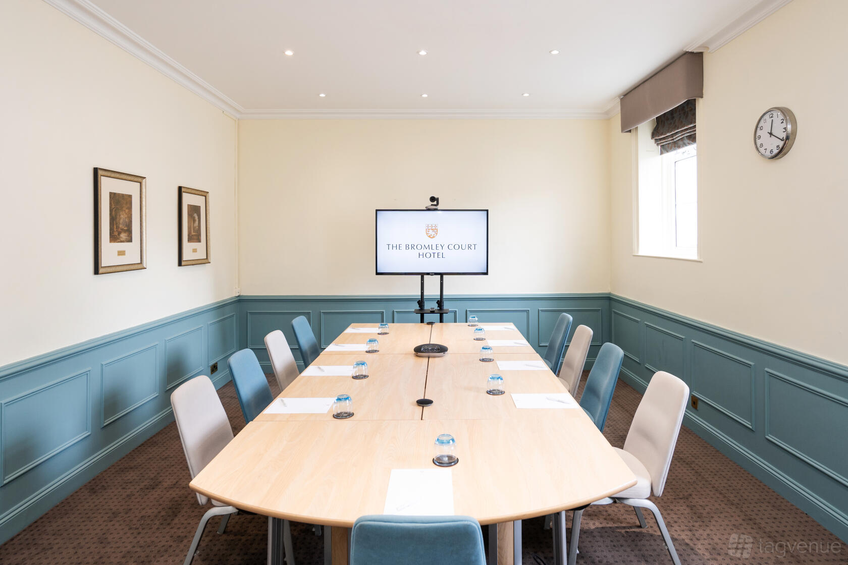 A hotel meeting room with a long rectangular table, conference chairs, a wall-mounted screen, and framed artwork at The Bromley Court Hotel.