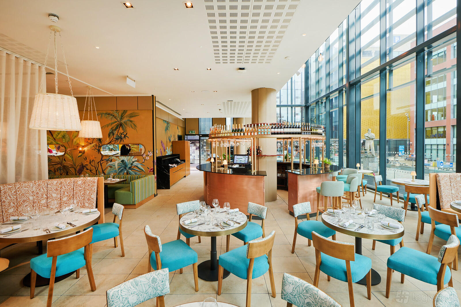 A dining room with floor-to-ceiling windows, colorful chairs, and round tables at Gino D'Acampo Manchester.