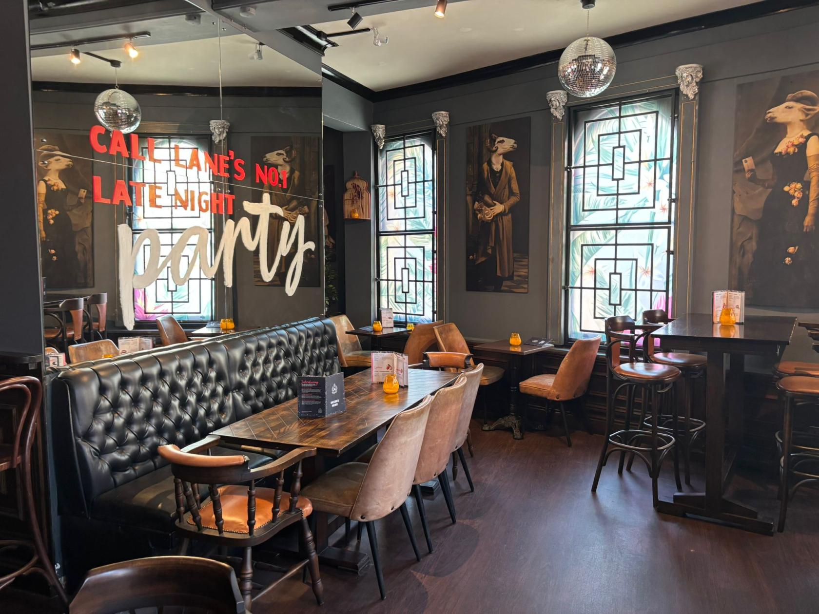 A cocktail lounge with leather banquette seating, disco balls, large windows, and animal portraits at The Maven.