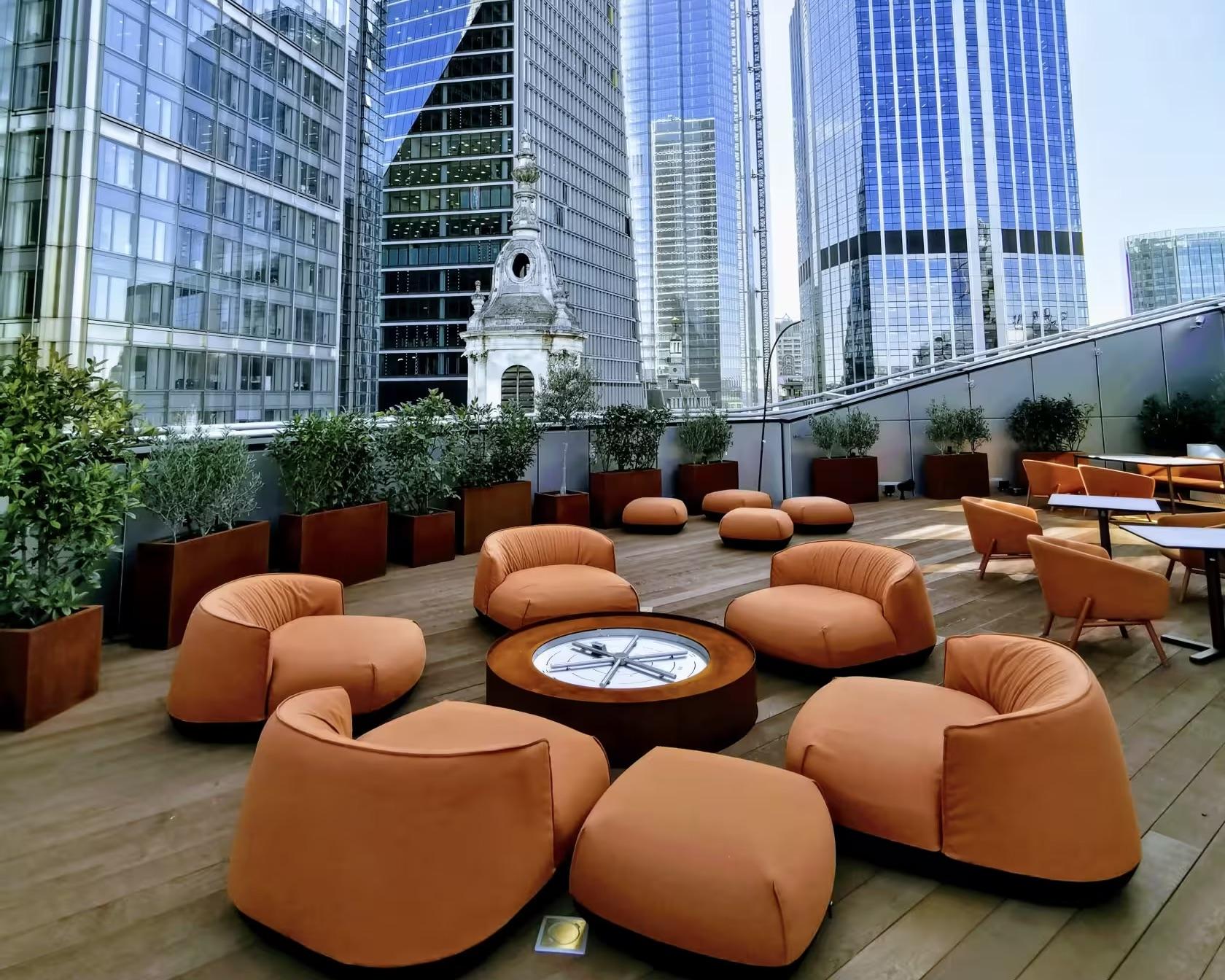 A coworking terrace with orange lounge chairs, round fire pit, and potted greenery at Uncommon Liverpool Street.