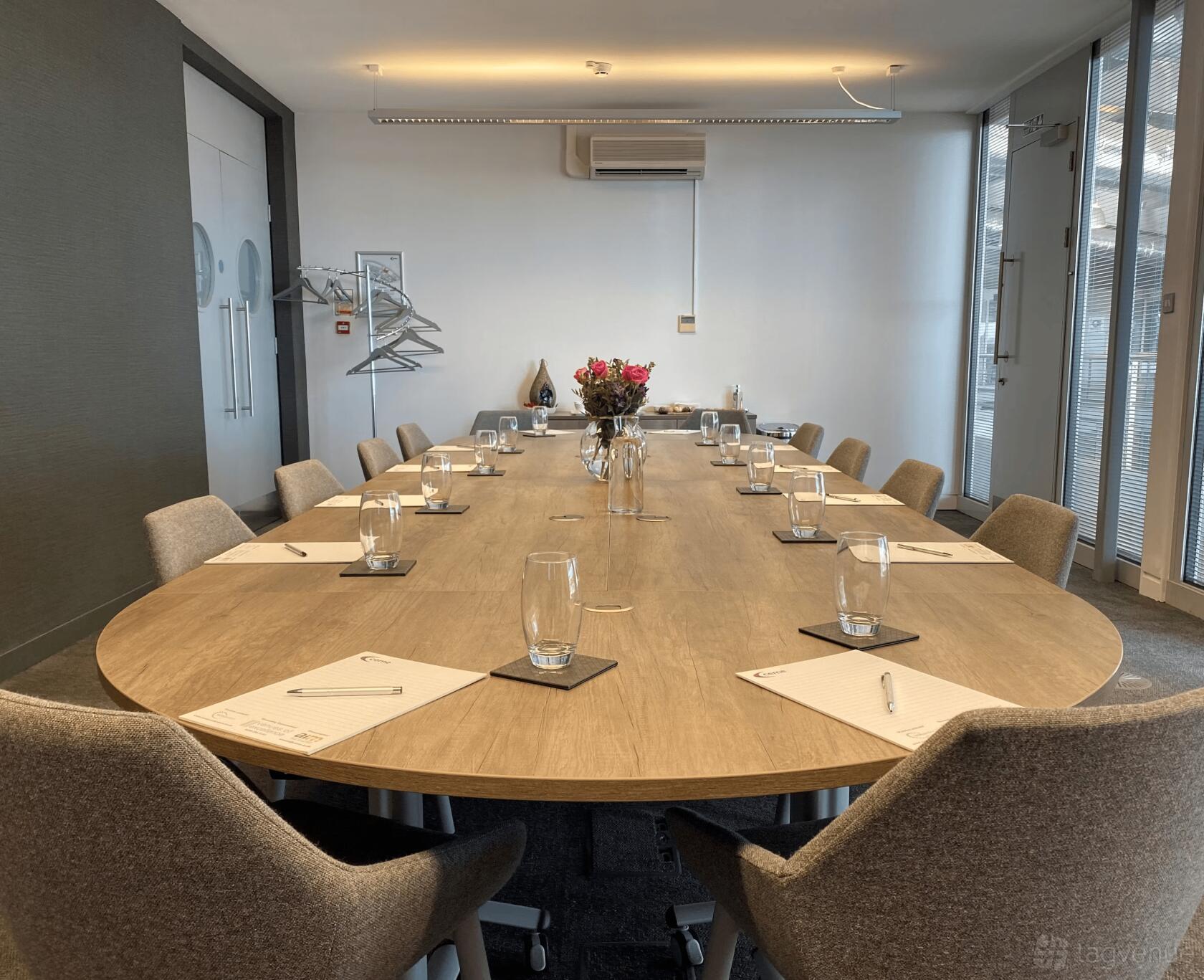 A meeting room with an oval boardroom table, grey chairs, glassware, and notepads at Event Space CEME.