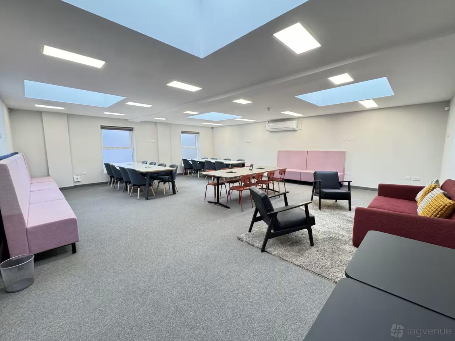 A training room with skylights, multiple tables with chairs, and soft seating at Collaborative One - Flexible Spaces.