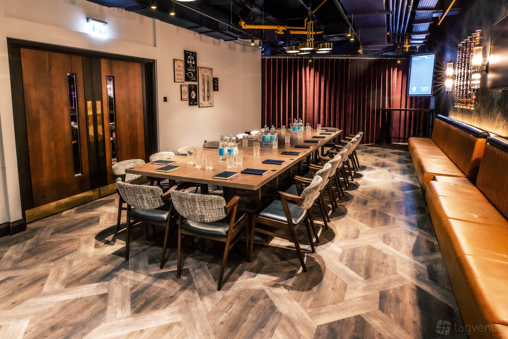 A meeting room with a long conference table, cushioned chairs, notepads, and a leather banquette at Puttshack Watford.
