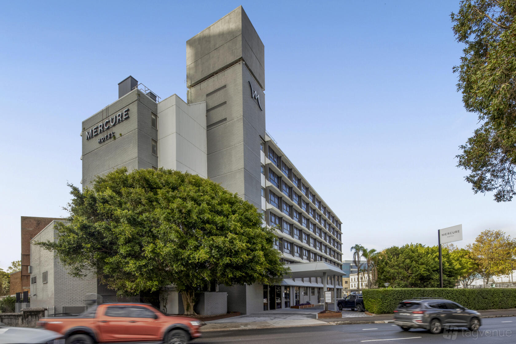 A hotel building with a multi-story facade, street-facing entrance, and large tree at Mercure Newcastle.