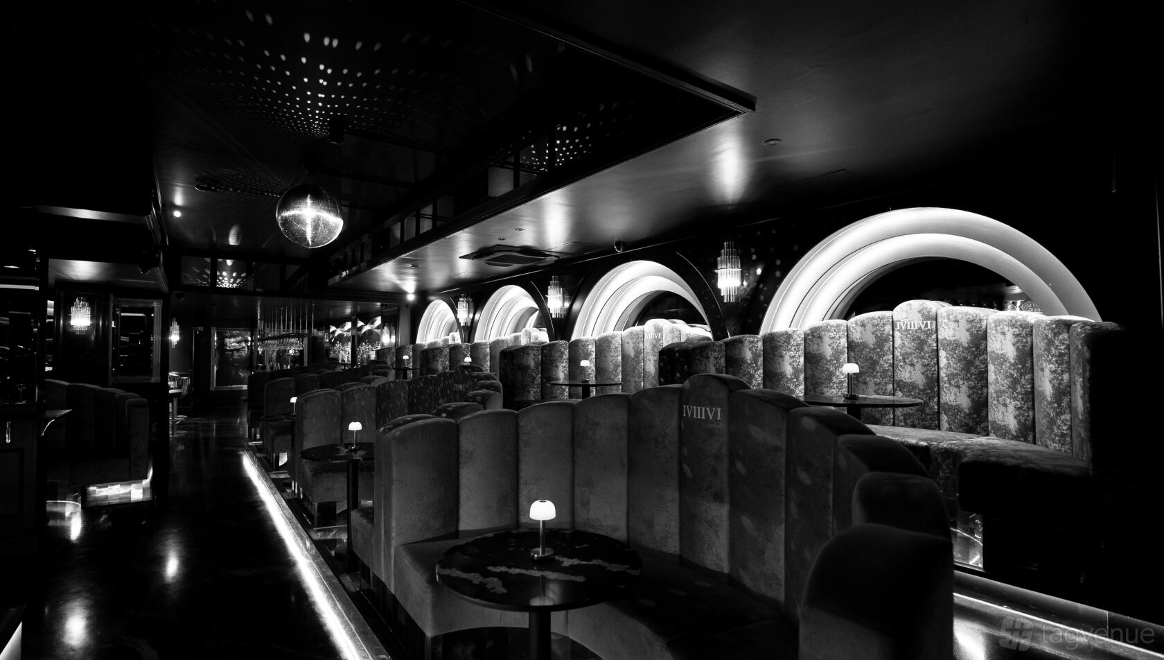 A bar with plush velvet booth seating, round tables with small lamps, and arched backlit windows at One Eight Six.