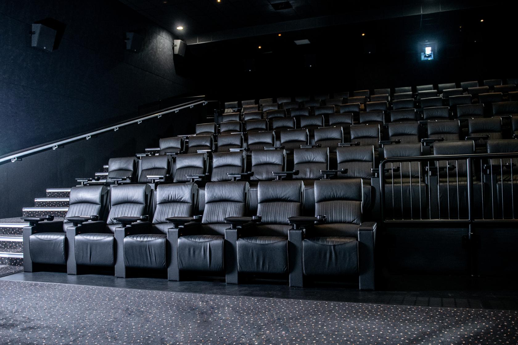 A cinema auditorium with tiered rows of black leather seats and carpeted steps at Vue Islington.