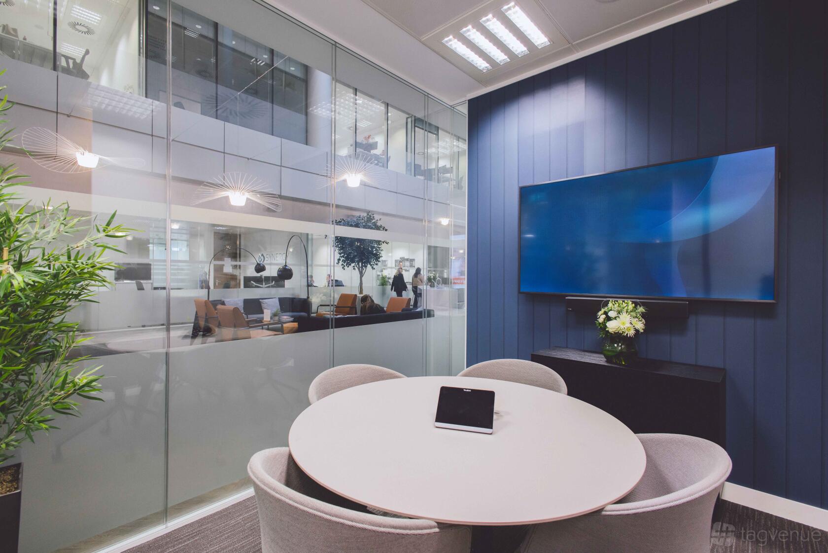 A boardroom with a round table, wall-mounted screen, and glass walls at Orega Gracechurch Street.