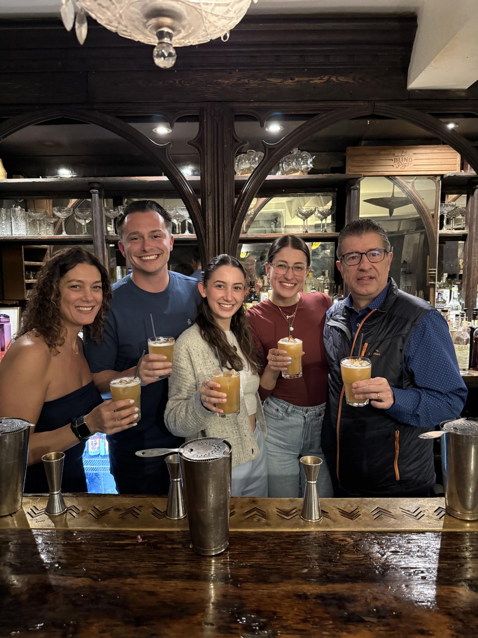 A cocktail bar with patrons holding drinks at a wooden counter at The Lucky Pig Cocktail Bar.