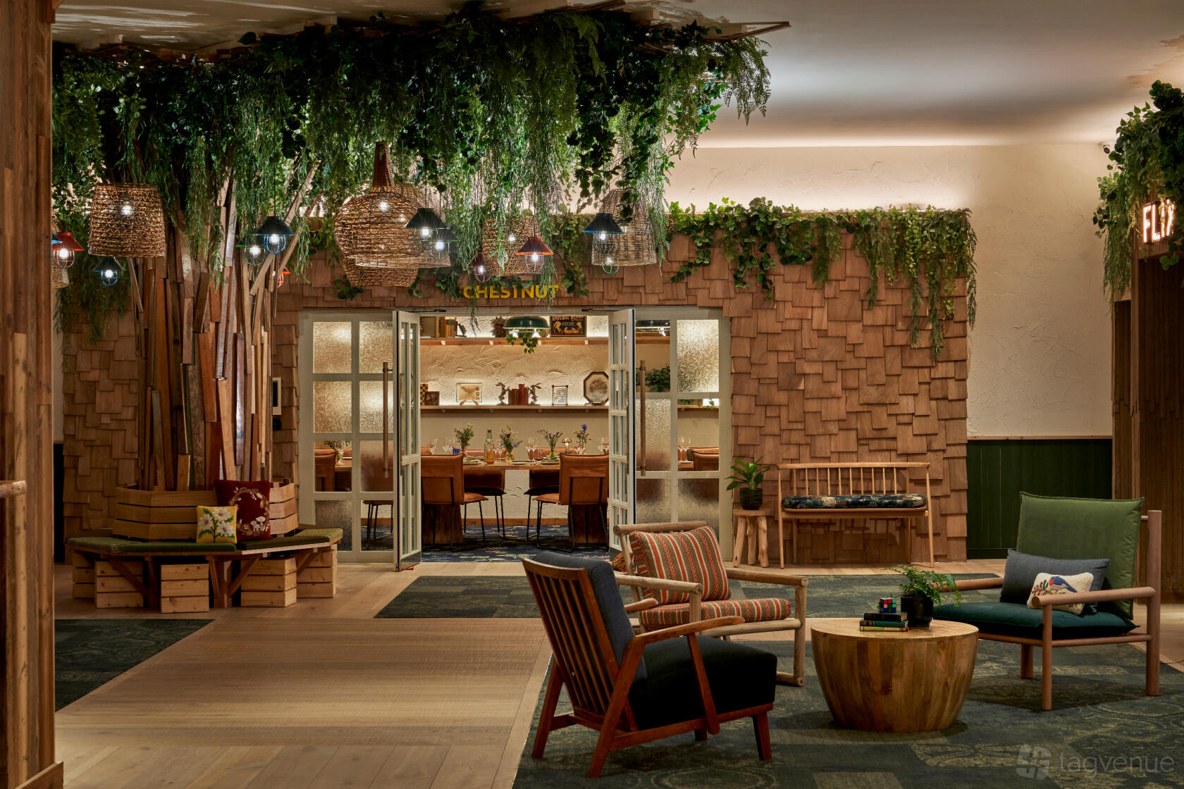 A hotel lounge with hanging greenery, wood-paneled walls, and a glimpse into a dining room at Treehouse Hotel Manchester.