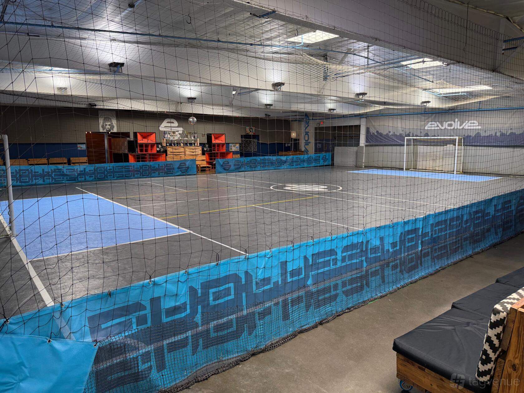 An indoor event venue with a full-sized futsal court, high ceilings, and spectator seating at Evolve Project LA.