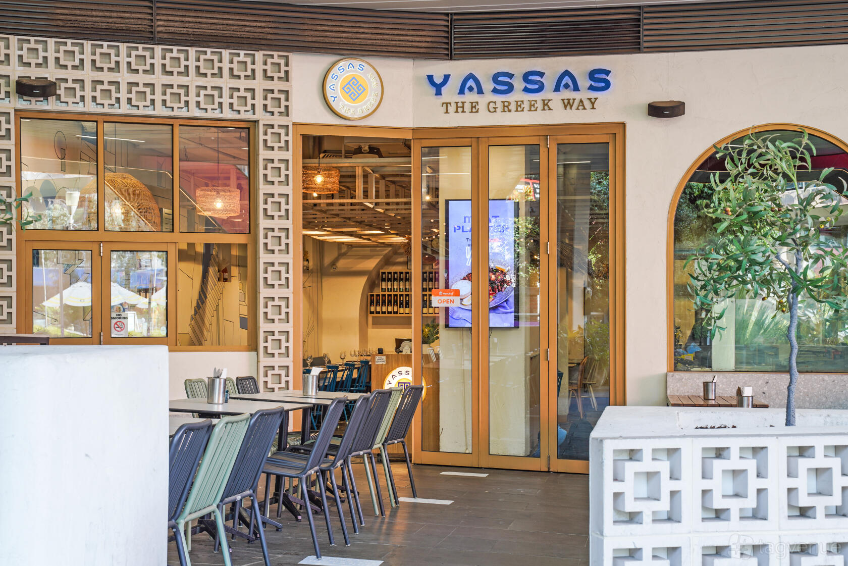 A restaurant entrance with glass doors, outdoor seating, and patterned wall accents at YASSAS - The Greek Way - Docklands.