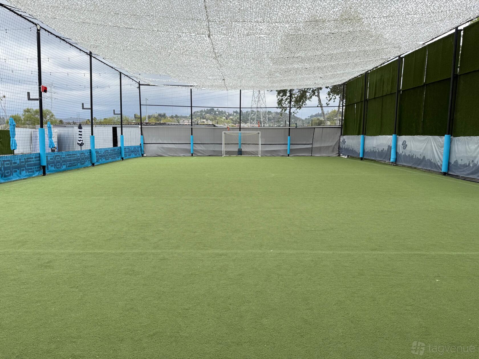 An outdoor event venue with artificial turf, mesh shade covering, and netted walls at Evolve Project LA.