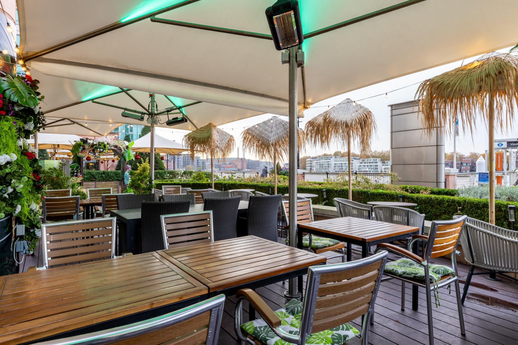 An outdoor event space with wooden tables, metal chairs, and thatched umbrellas at Cottons Vauxhall.