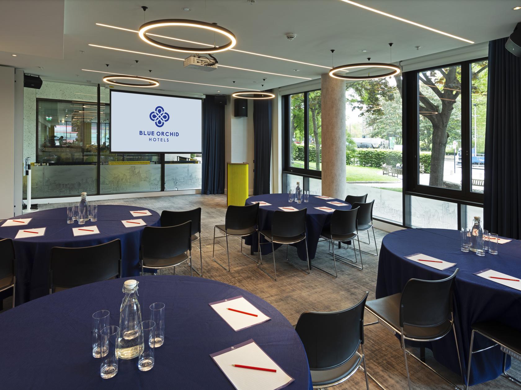 An event space with round tables covered in navy linens, black chairs, and a projector screen at Tower Suites by Blue Orchid.