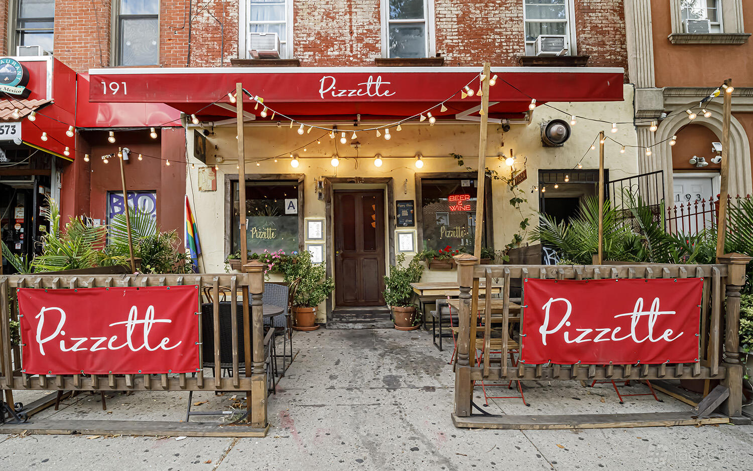 A restaurant with outdoor seating, string lights, red awnings, and greenery at Pizzette.