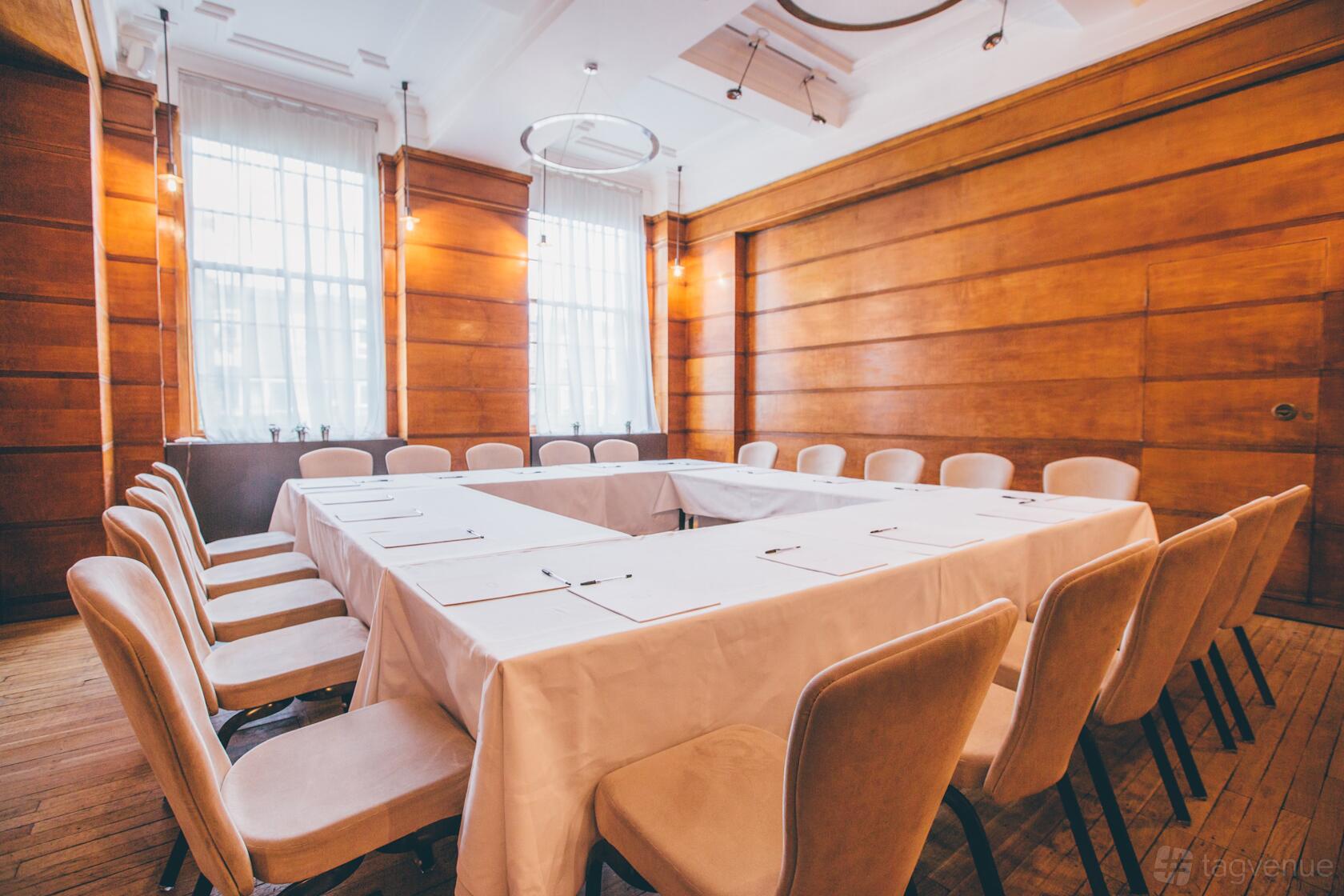 A function room with wood-paneled walls, large windows, and U-shaped table with beige chairs at Town Hall Hotel.