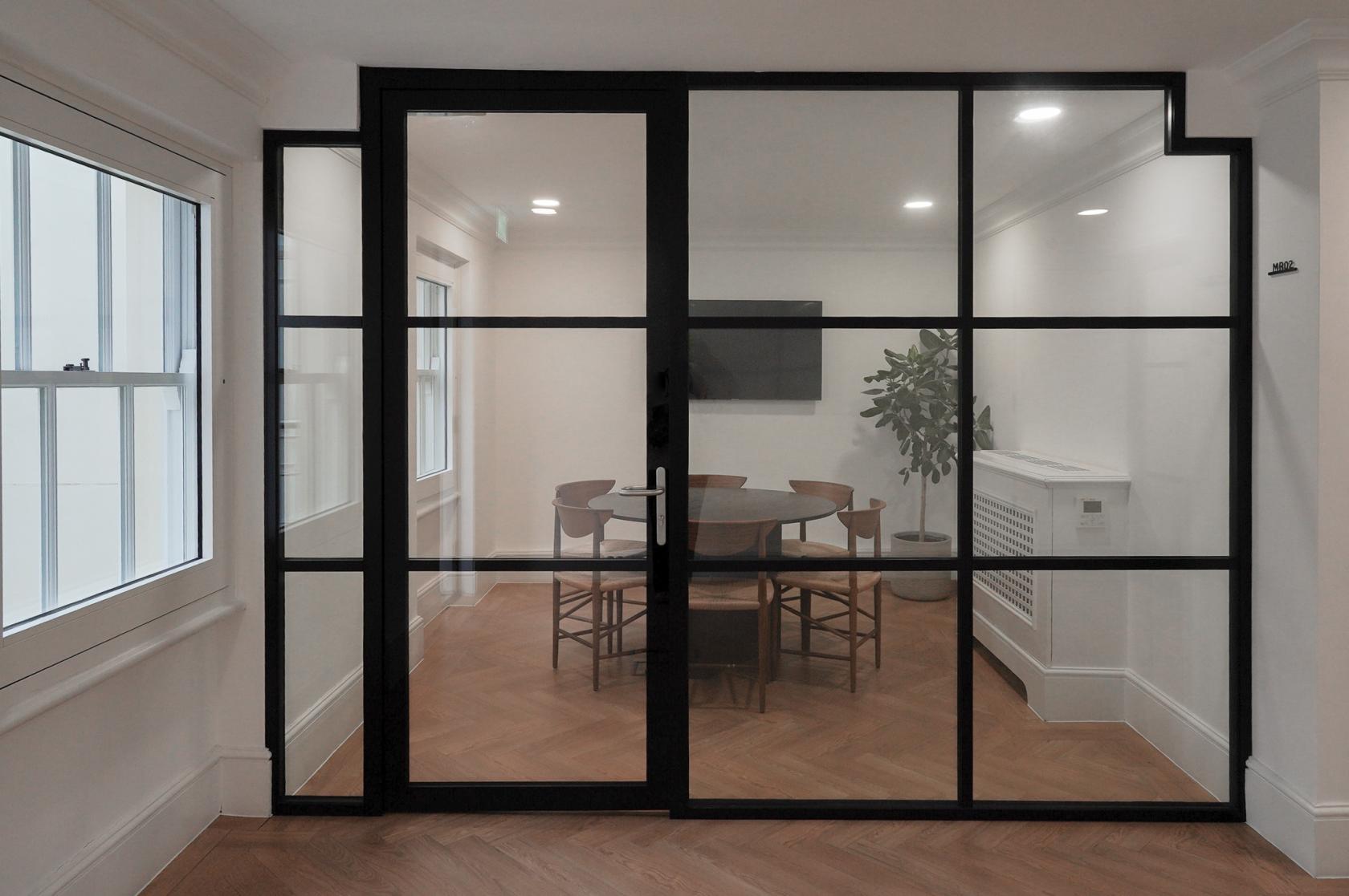 A meeting room with glass walls, round wooden table, chairs, wall-mounted screen, and potted plant at WorkPad: 22 King Street.
