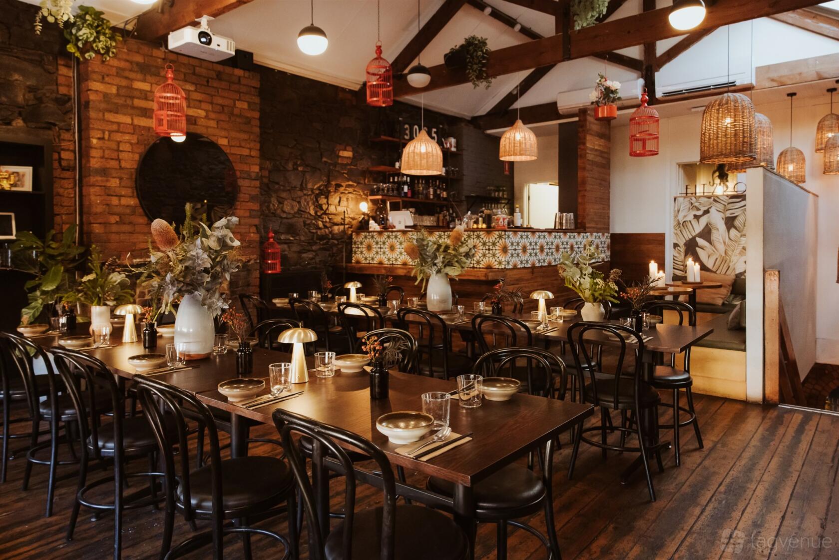 A function room in a restaurant with exposed brick walls, wooden tables, and hanging woven pendant lights at Rice Paper Scissors Fitzroy.