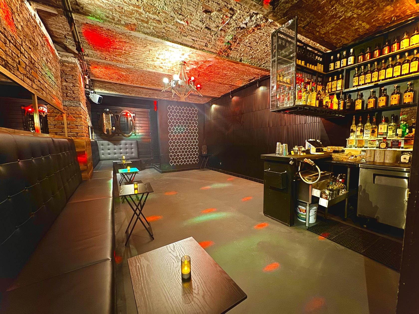 A bar with exposed brick ceiling, tufted banquette seating, dark walls, and a stocked bar at Whiskey Cellar NYC.