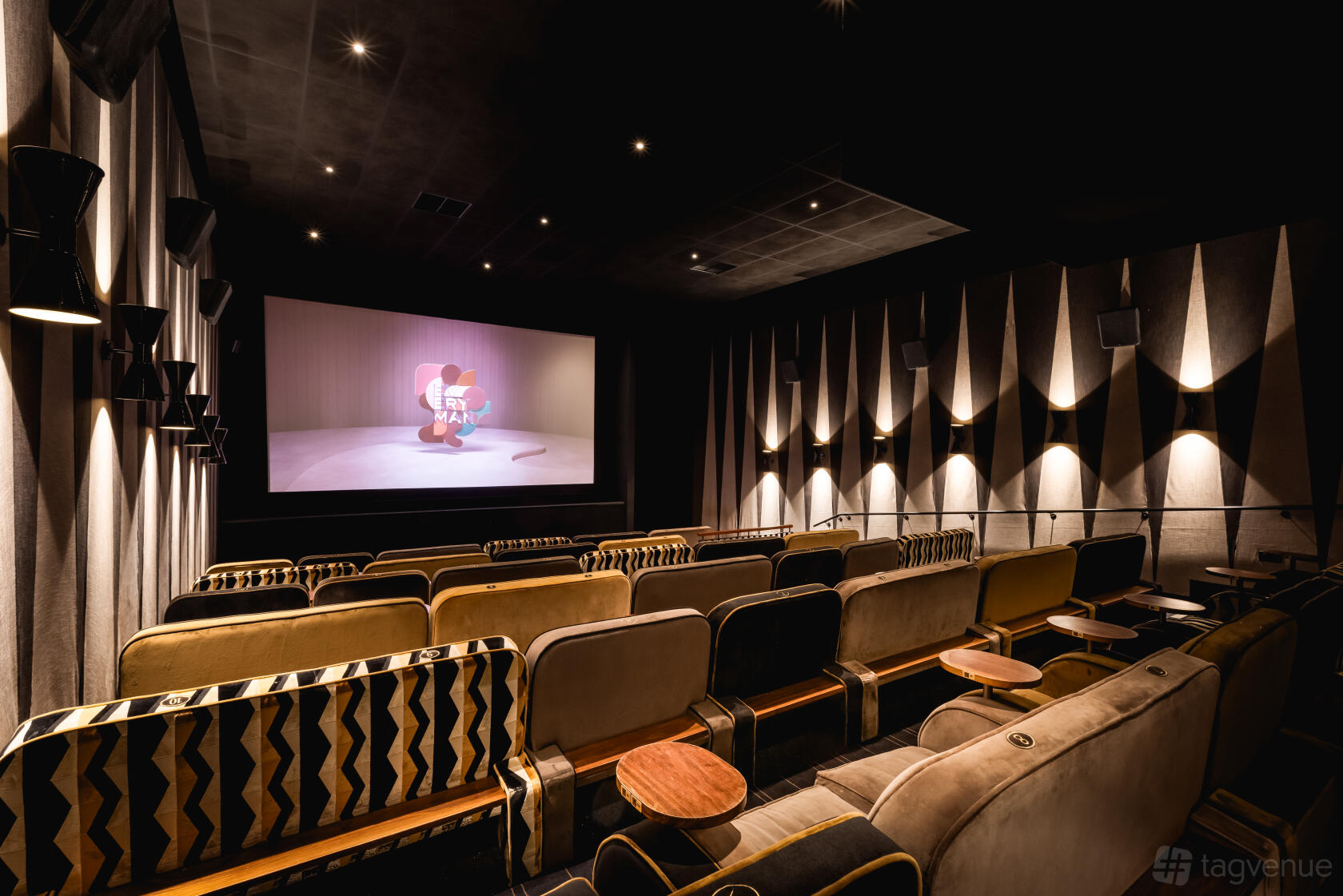 An auditorium with plush armchairs, side tables, and wall-mounted lighting facing a large screen at Everyman Stratford-Upon-Avon.