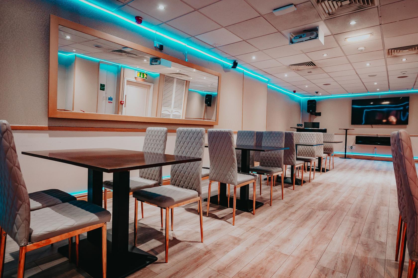 A dining room with upholstered chairs, rectangular tables, wood flooring, and blue accent lighting at Riverboat Casino.