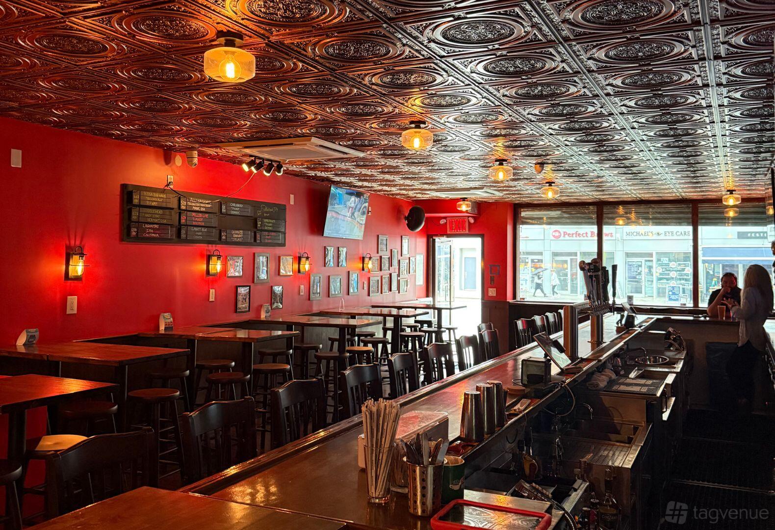A bar with a pressed tin ceiling, red walls, mounted televisions, and tall wooden tables at Kellys Sports Bar.