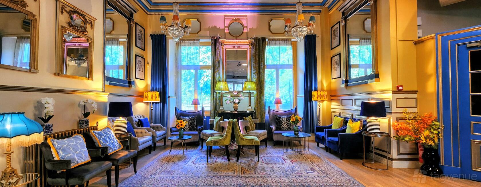 An event venue with tall windows, crystal chandeliers, elegant seating, and decorative mirrors at Lumiere London - The Embassy.