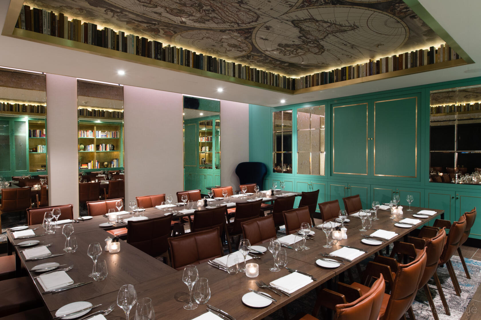 A private dining room with a large U-shaped table, leather chairs, teal bookcase walls, and a map ceiling at Vintry & Mercer.