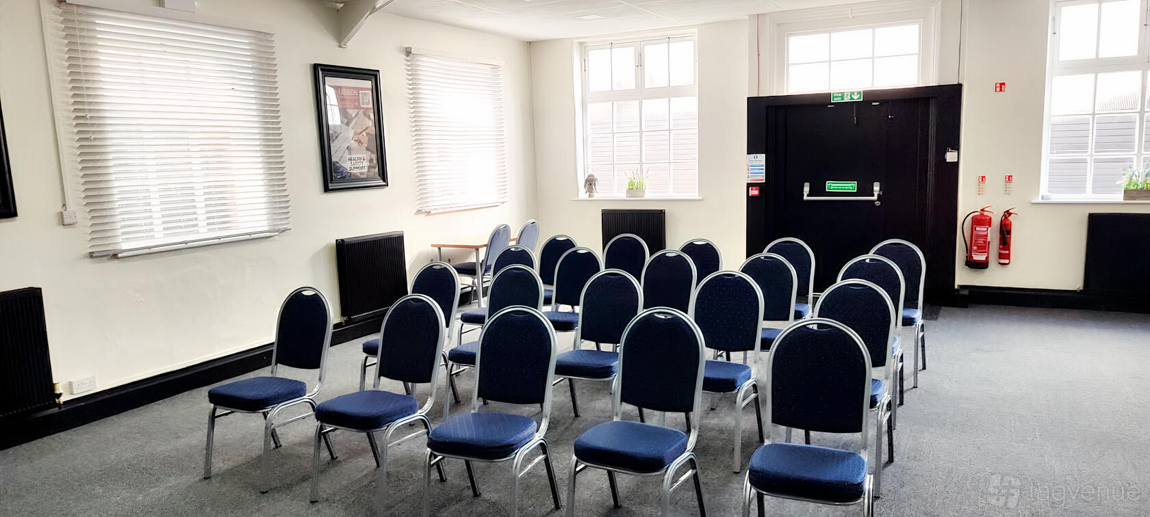 A meeting room with rows of blue cushioned chairs, large windows, and white walls at The Walsall Hub.