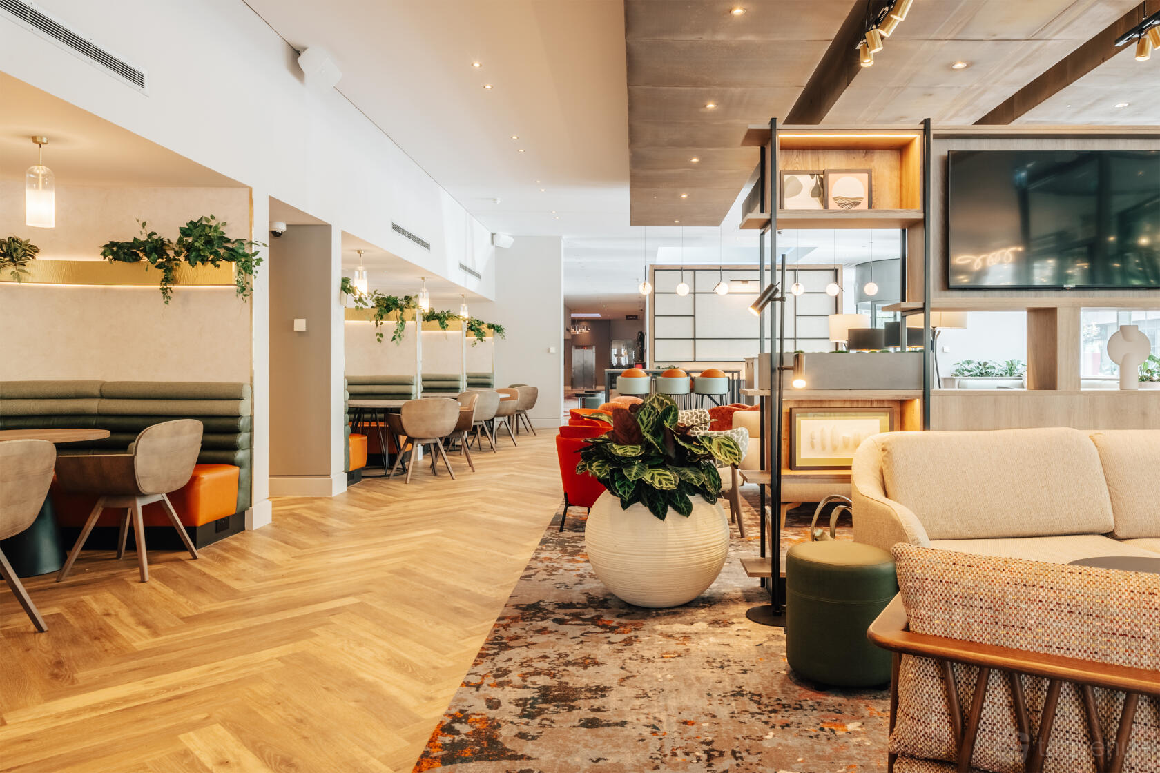 A lounge with wood flooring, soft seating, booth tables, and potted plants at Crowne Plaza London Docklands.