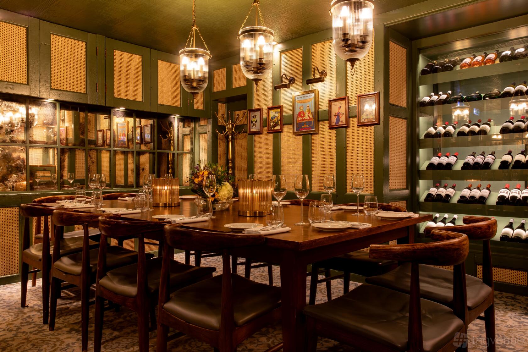 A private dining room with a long wooden table, wine display shelves, and framed art at Trishna.