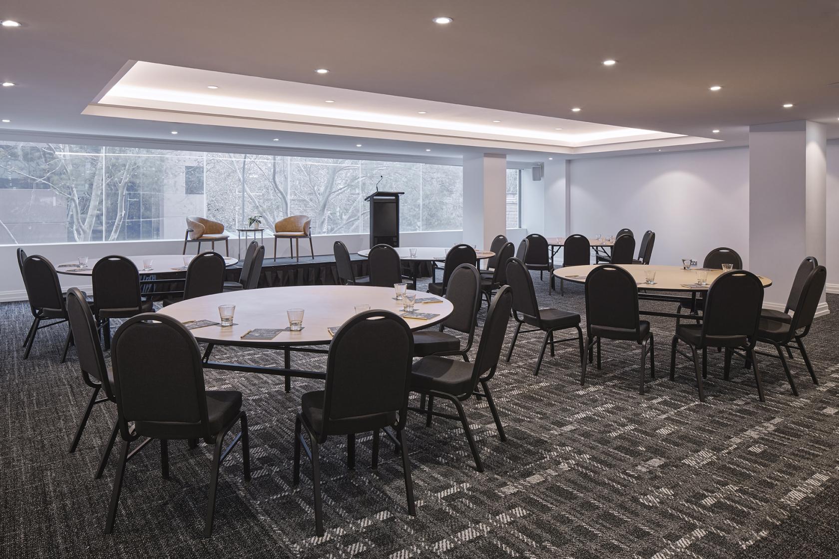 An auditorium with round tables, black chairs, carpeted floors, and large windows at Rydges Sydney Central.