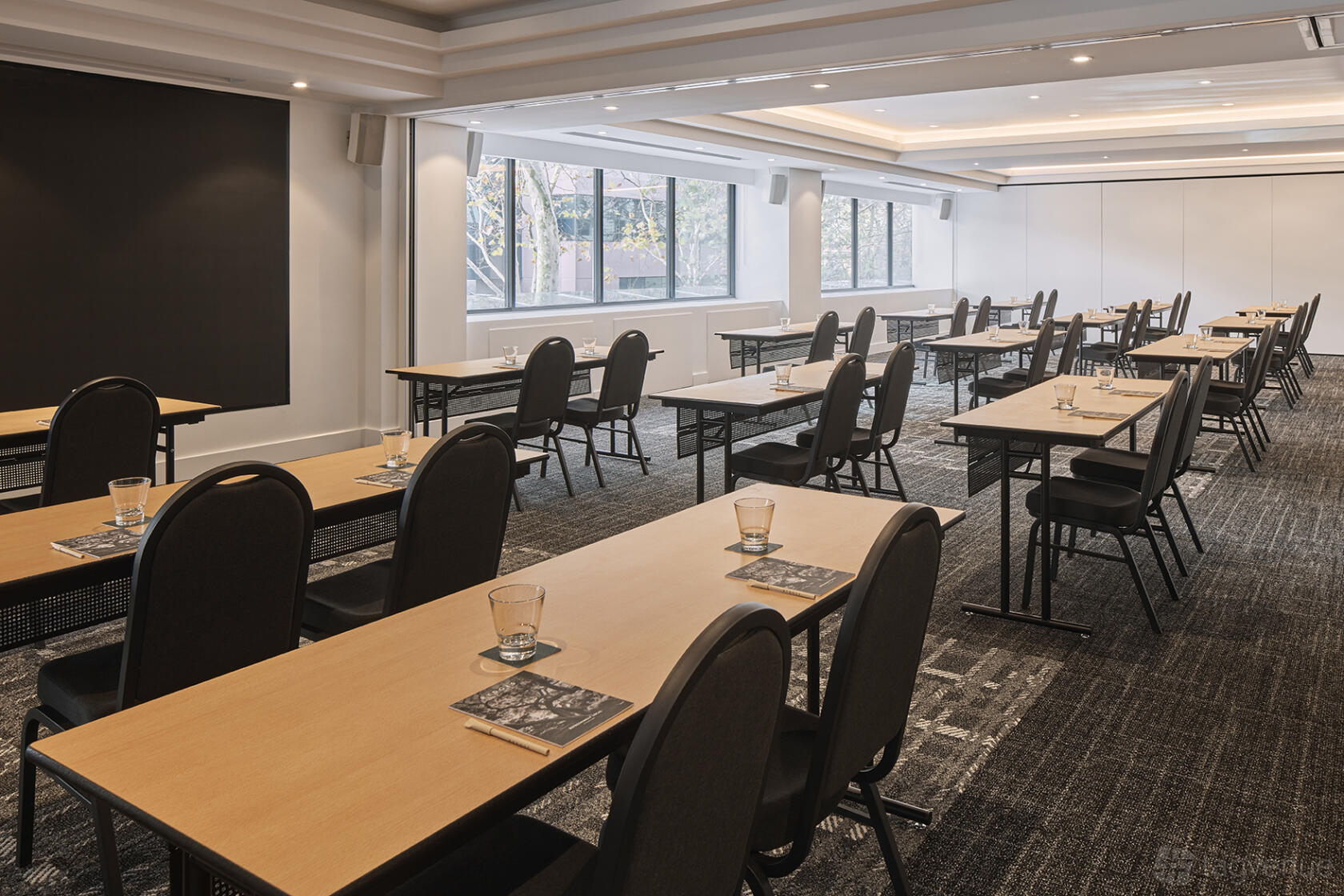 A meeting room with large windows, rectangular tables, and black chairs at Rydges Sydney Central.