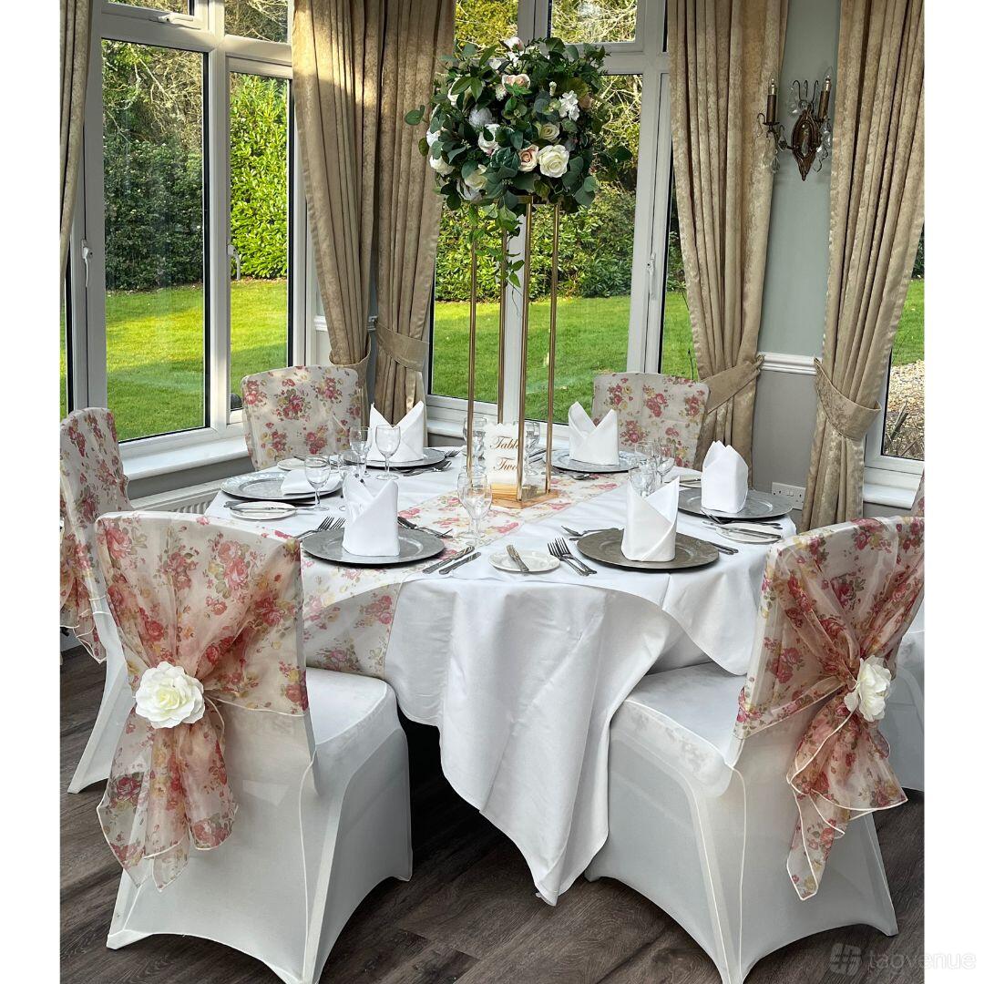 An event space with round tables dressed in white linens and floral chair covers beside large windows at Farnham House Hotel.