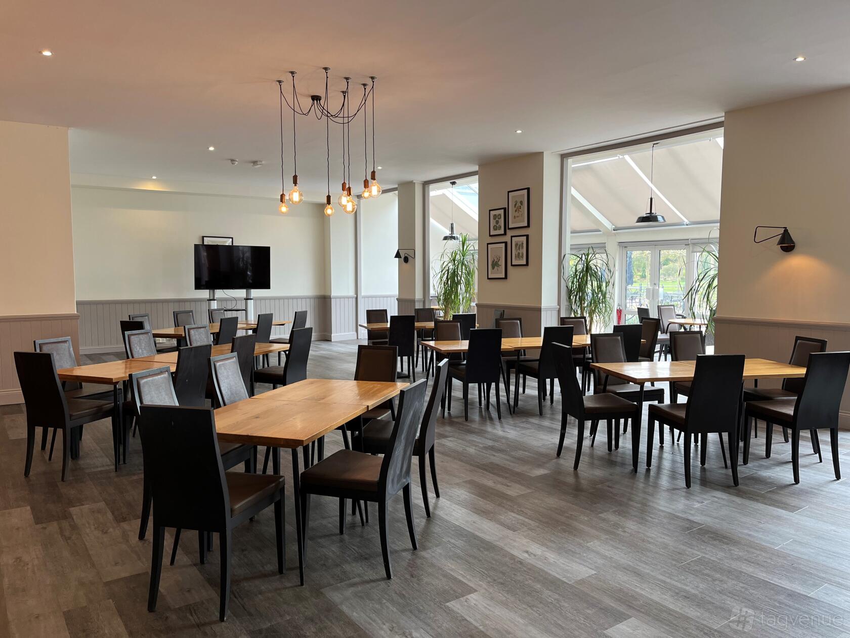 An event venue with large windows, wooden tables, black chairs, and hanging pendant lights at RHS Garden Wisley