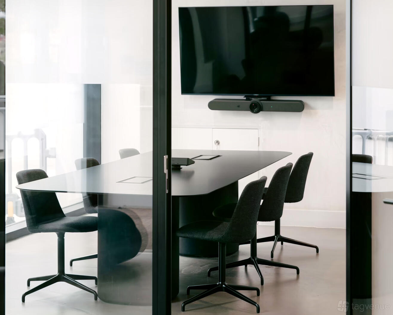 A meeting room with a large black conference table, six chairs, and a wall-mounted screen at Broadwick Studio.
