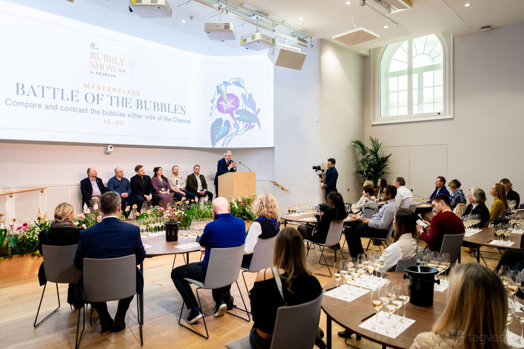 A hall with a stage, panel seating, floor-to-ceiling windows, and audience chairs at {10-11} Carlton House Terrace.