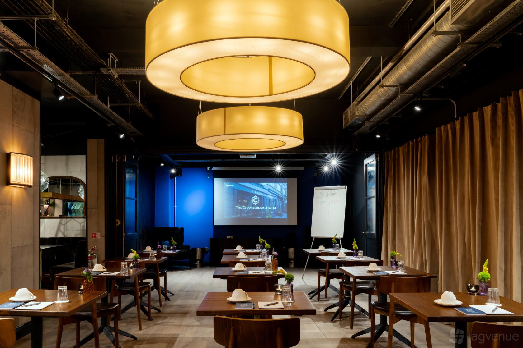 A meeting room with round pendant lights, individual tables, notepads, and a projector screen at The Chamberlain.