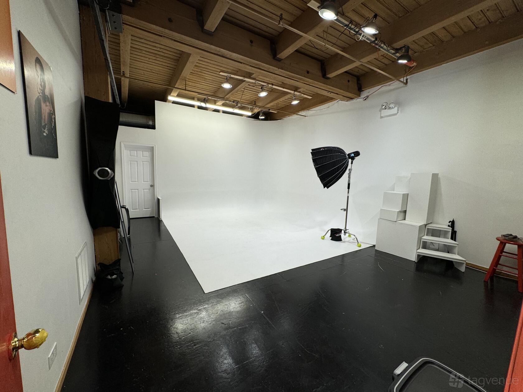 A photo studio with a white cyclorama wall, black floors, lighting equipment, and exposed wooden ceiling at Launchpad Studios.