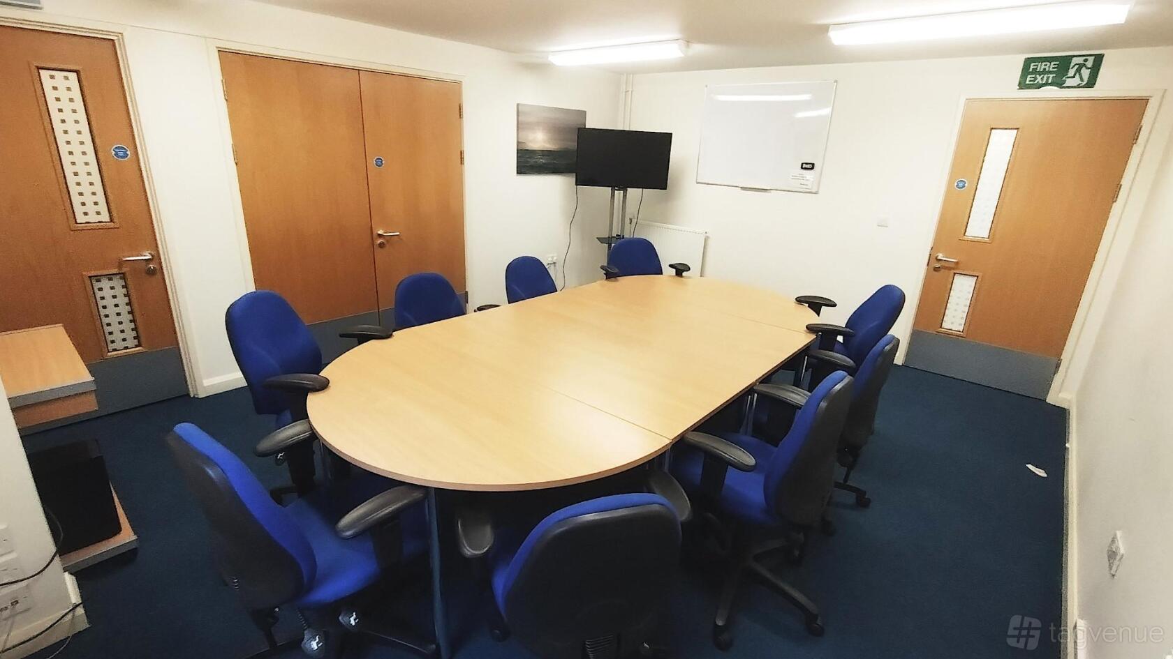 A meeting room with an oval conference table, blue chairs, a wall-mounted TV, and a whiteboard at Castleland Community Centre.